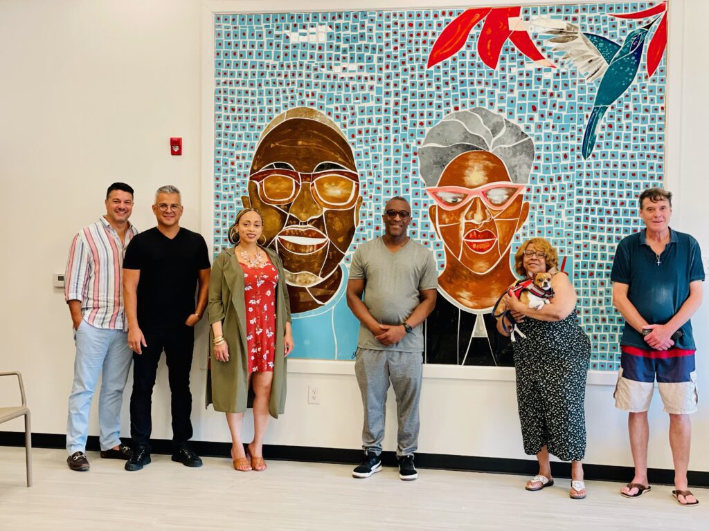 Group of smiling people standing in front of the Faces of Diversity mural