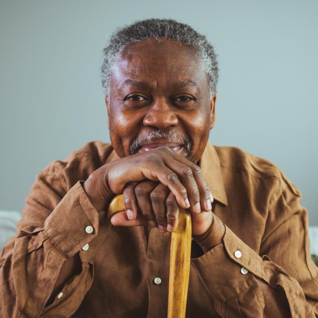 Mature African American man sitting and resting his hands on his cane
